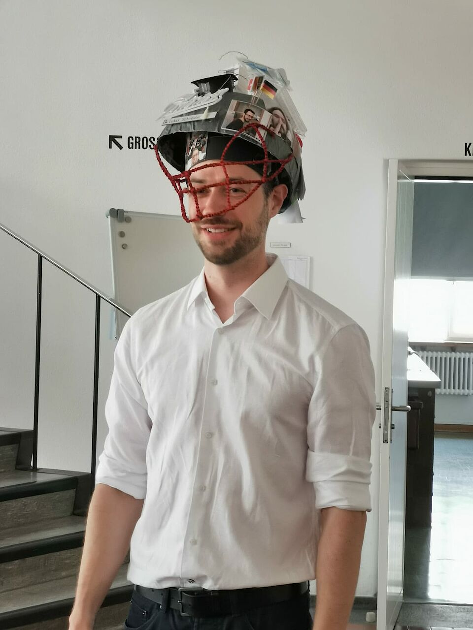 Dr Lukas Schneider wearing his hat after his successful oral examination. The hat looks like a football helmet dyed in the colors of the patriots.